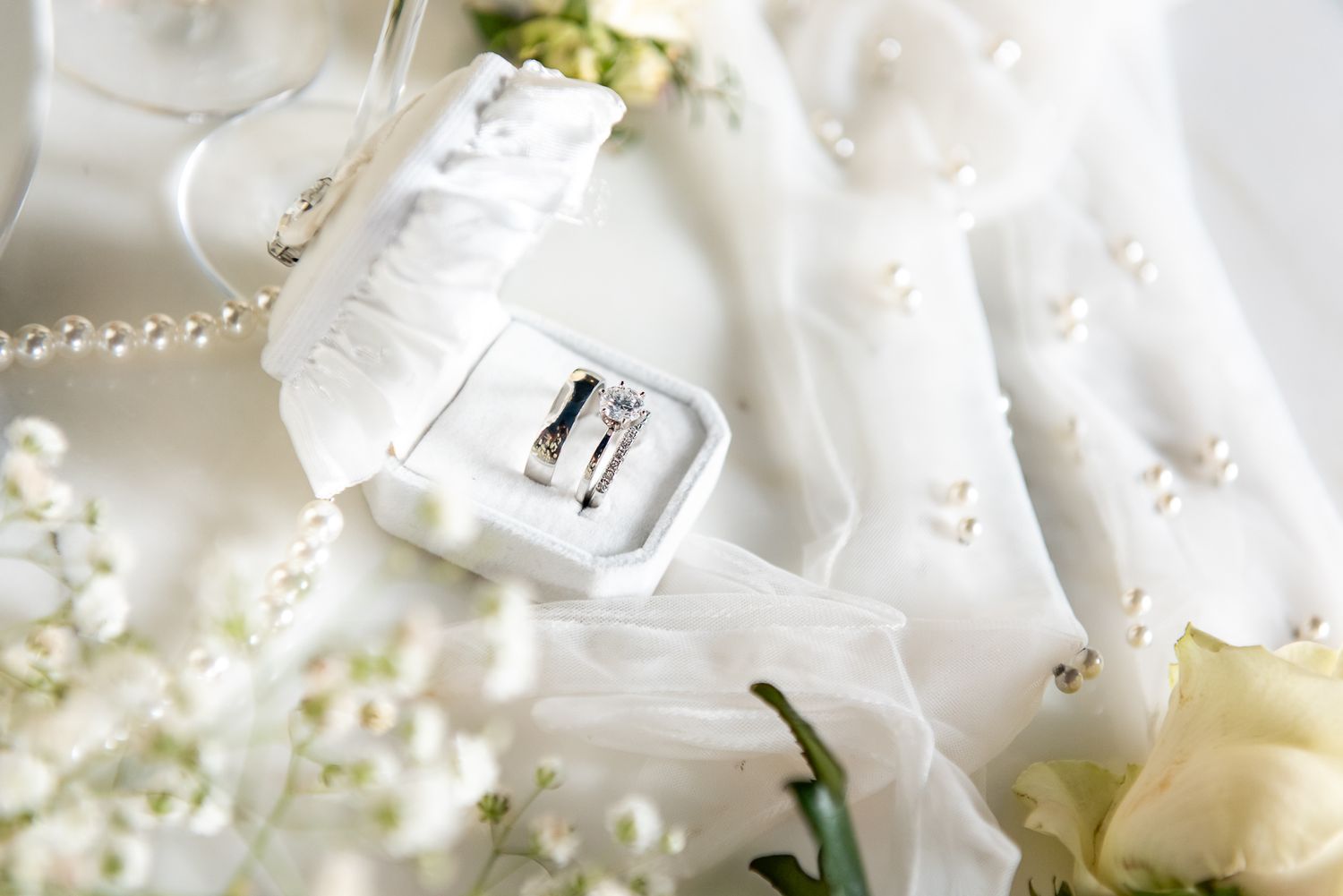 Close-up of wedding accessories with white roses and pearls on satin fabric.