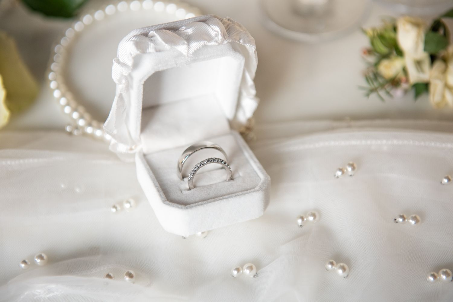Elegant white wedding accessories and pearls arranged on white fabric.