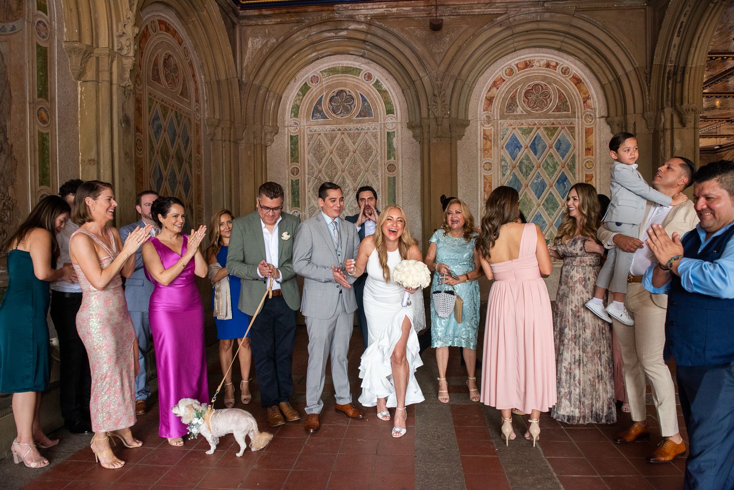 Wedding guests dance and celebrate in an ornate ballroom with decorative walls and arches.
