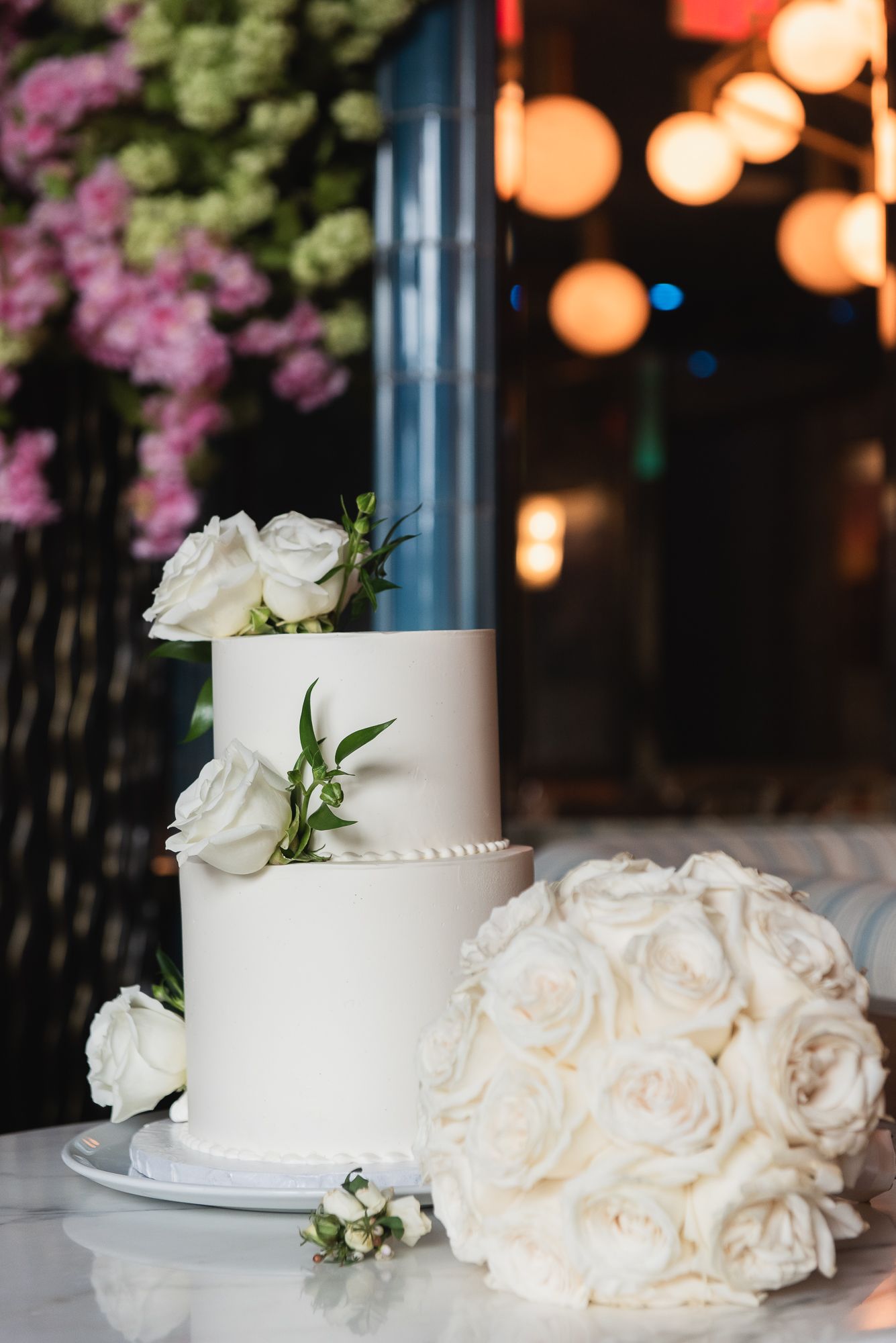 Elegant white wedding cake decorated with fresh roses and soft lighting.