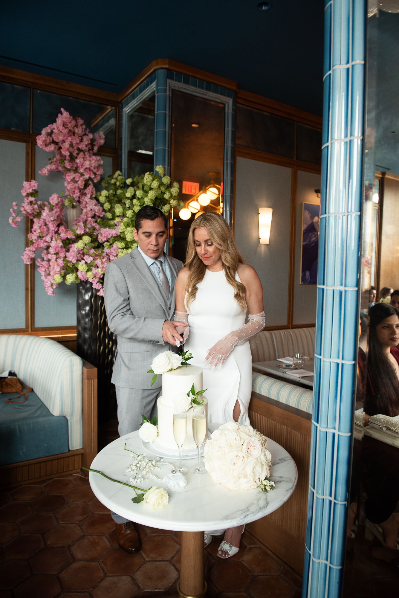 Newlyweds standing beside their elegant white tiered wedding cake at reception venue.