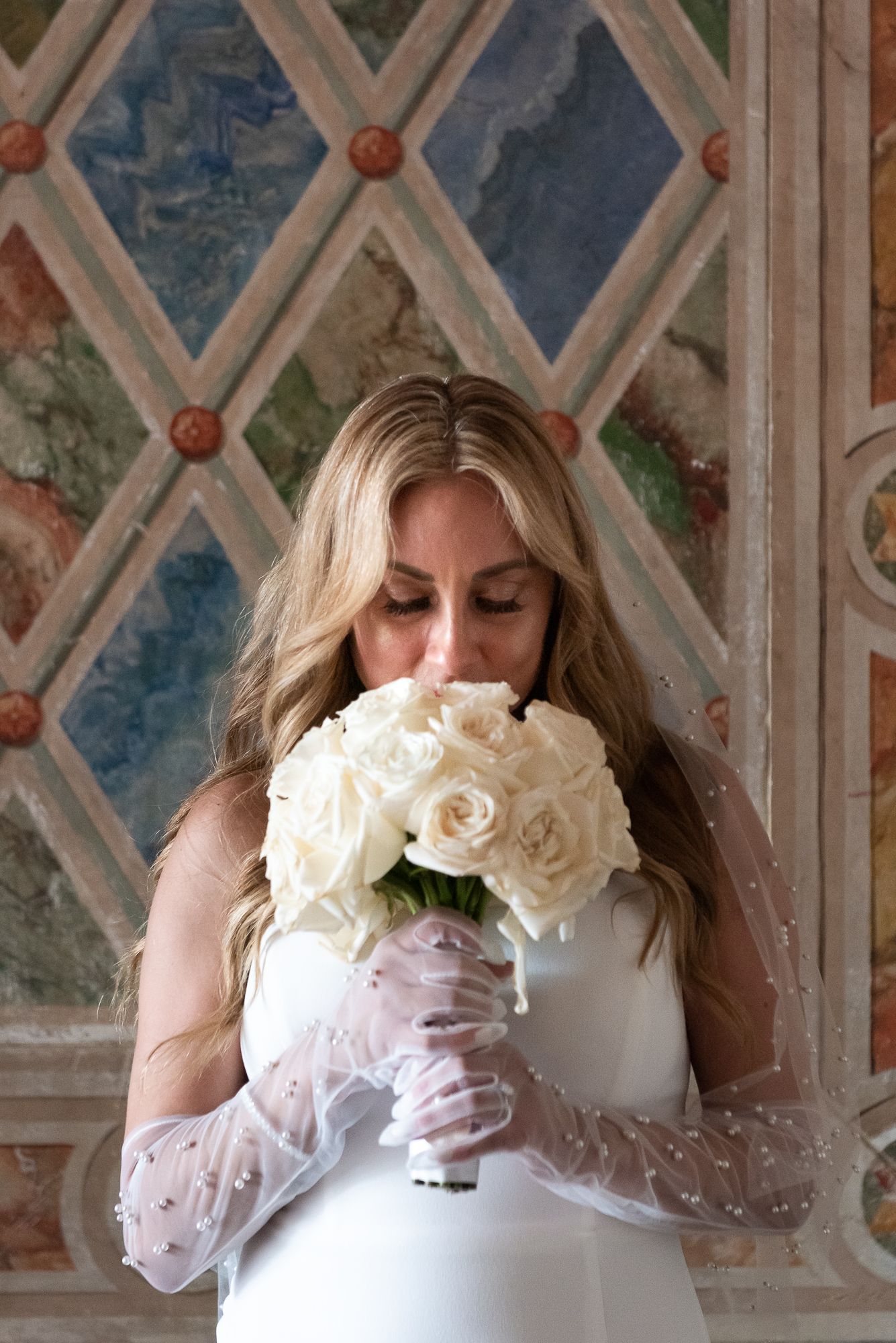 Romantic bridal portrait with white roses bouquet against ornate painted wall.