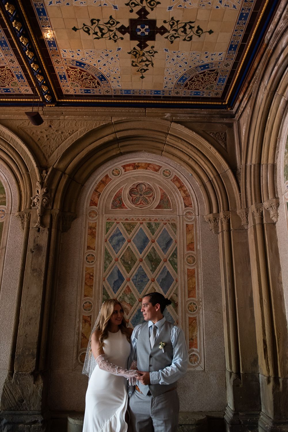 Wedding couple posing under ornate architectural details with diamond-patterned ceiling designs.