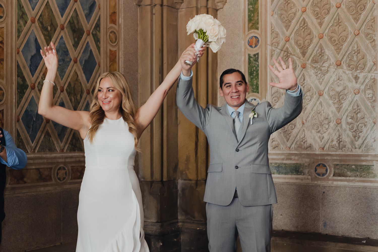 Couple celebrates joyfully in front of a decorative wall with vintage diamond patterns.