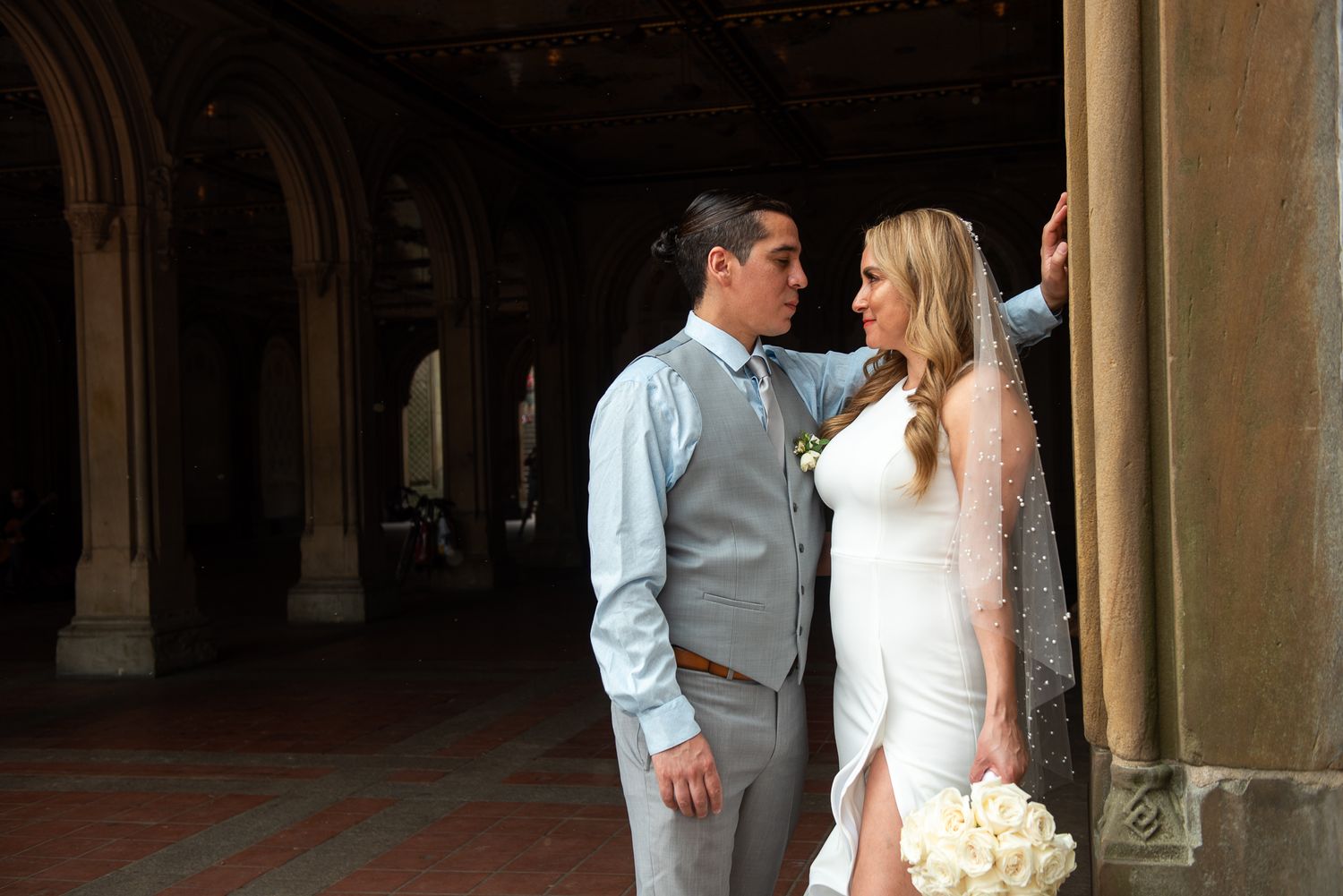 Wedding couple poses for portraits in dramatic historic hallway setting.