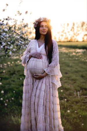 Ethereal sunset maternity portrait in flowing tiered dress among spring blossoms.