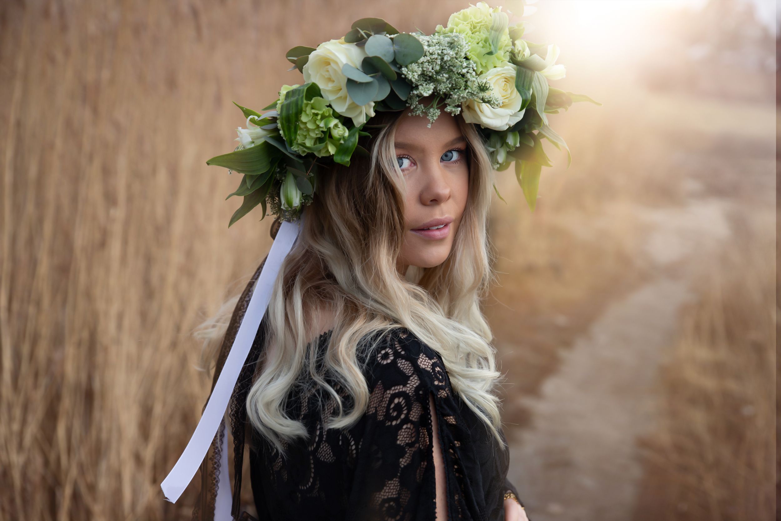 Whimsical maternity portrait with green floral crown and black lace dress in wheat field.