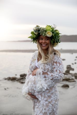 Maternity beach photo with woman in white lace dress wearing green and white floral crown.