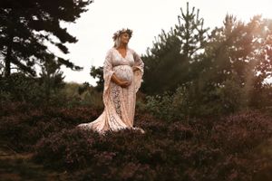 Romantic maternity photography in a white bohemian dress against a forest backdrop at golden hour.