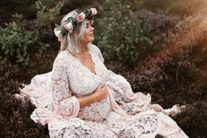 Bohemian style maternity photo with intricate lace dress and floral crown amidst nature.