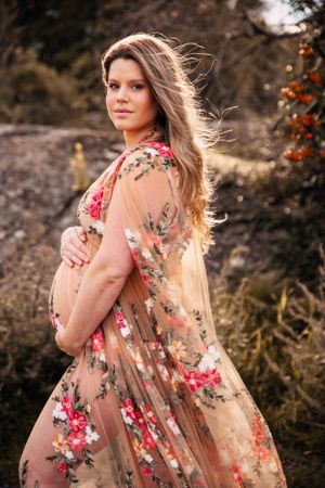 A flowing floral maxi dress in peach tones moves gracefully in a golden hour outdoor maternity photoshoot.