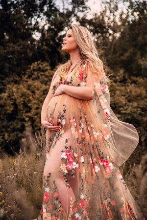 Ethereal maternity portrait featuring a sheer floral dress with pink blooms captured in natural outdoor lighting.