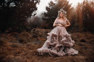 Dreamy maternity portrait showcasing a flowing mauve ruffled dress in a misty forest setting.