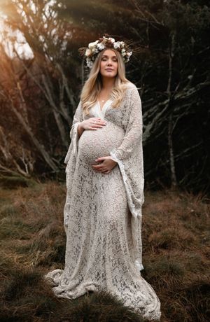 Ethereal maternity portrait featuring a white lace dress and floral crown in a wooded setting at sunset.
