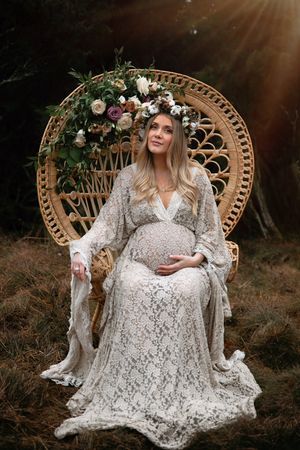 Elegant maternity portrait on a wicker peacock chair adorned with flowers and greenery.