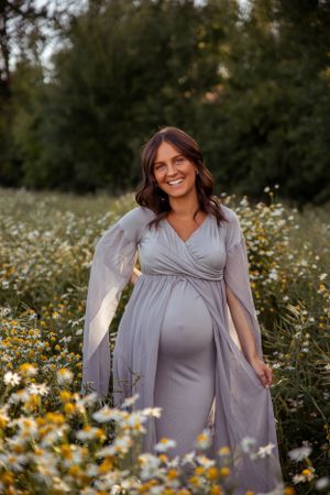 Maternity portrait featuring woman in grey dress surrounded by wildflowers.