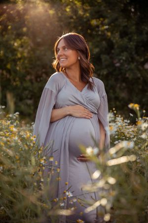 Candid maternity portrait in grey dress amid sunlit wildflower field.