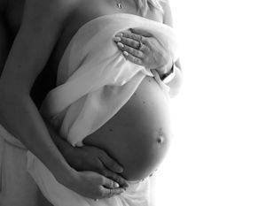 Intimate black and white maternity photo highlighting pregnant belly with gentle hands.