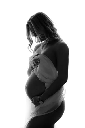 Artistic black and white maternity silhouette showing pregnant figure in soft light.
