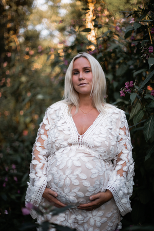 Expectant mother in white lace dress poses in garden with autumn colors.