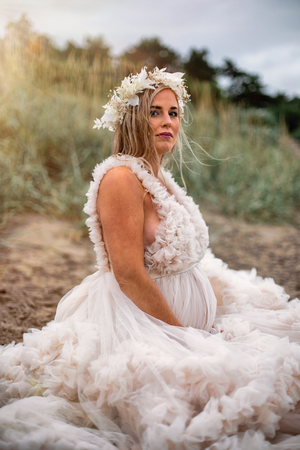 White flowy dress and floral crown create ethereal maternity portrait outdoors.