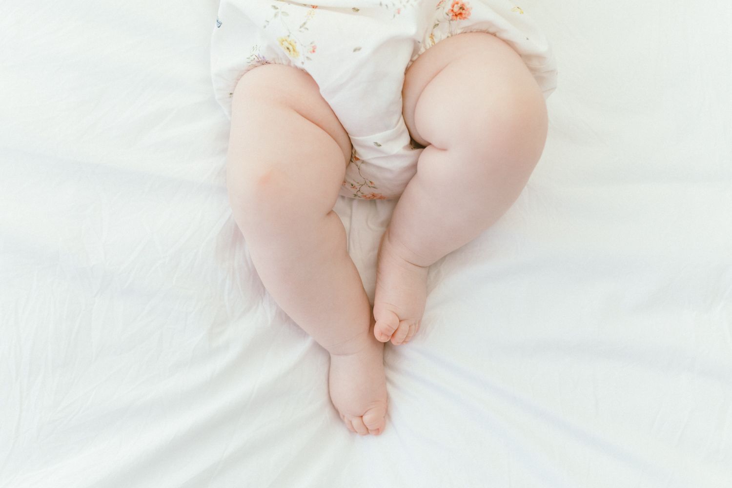 Close-up view of baby legs and feet on white fabric.