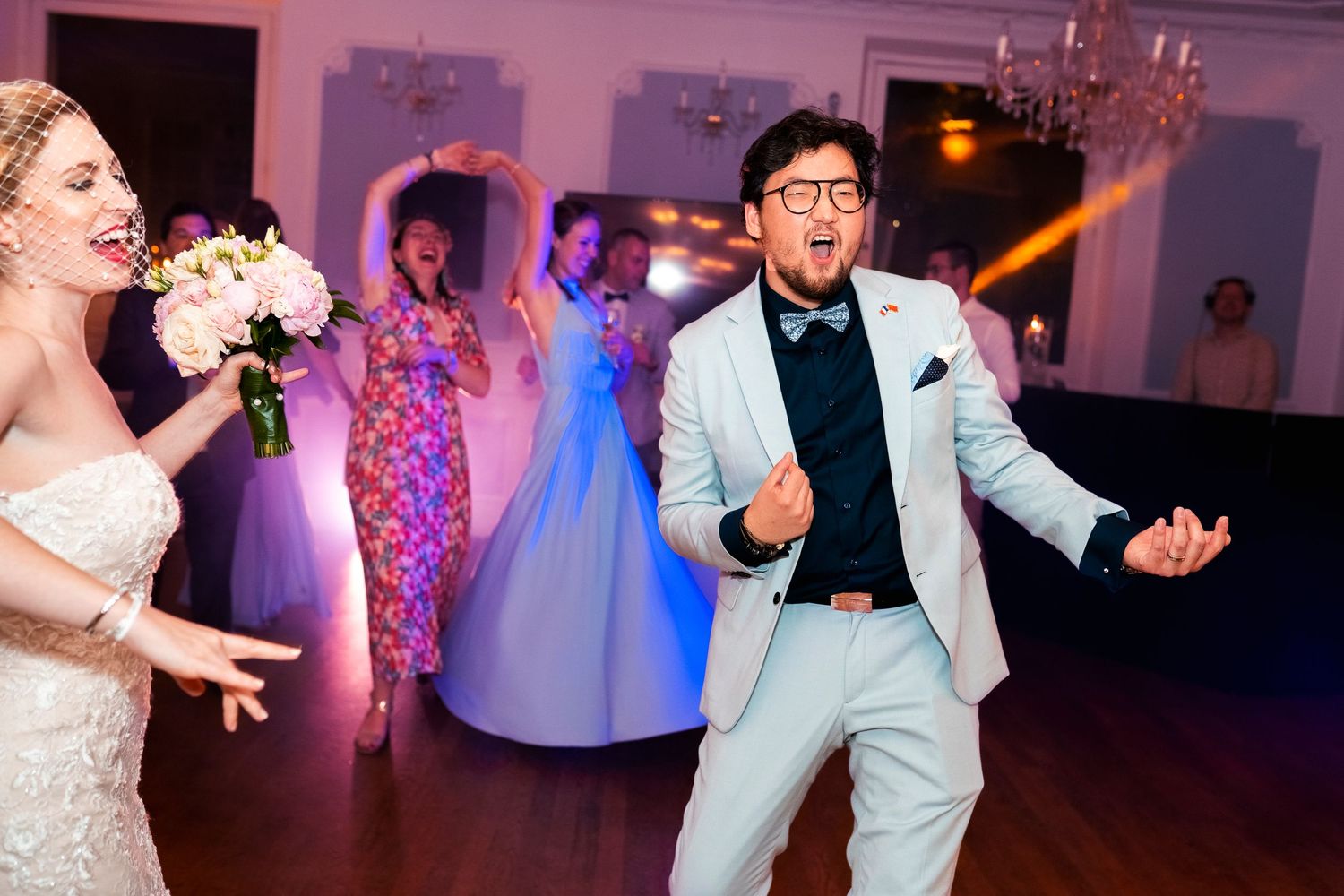 Wedding guests dancing and celebrating on a purple-lit dance floor.