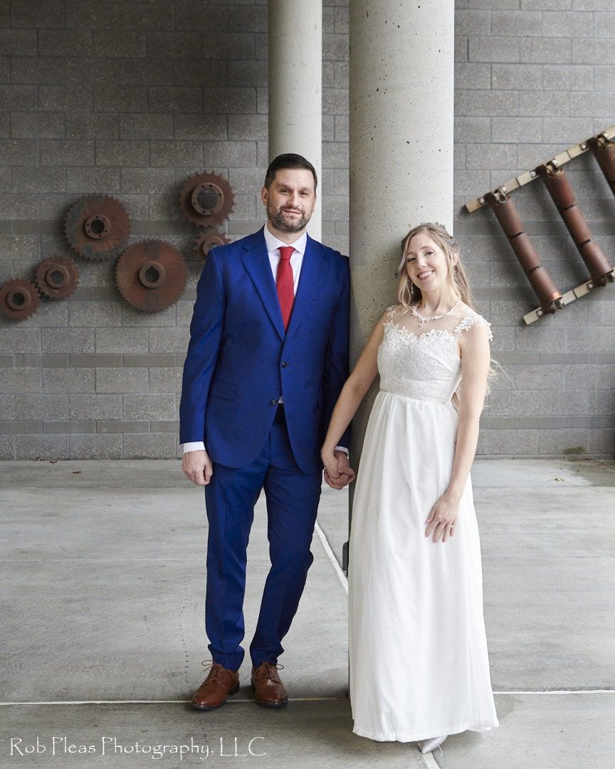 Bride and Groom formal holding hands leaning against pillars at Tacoma Environmental Services Building near Chambers Bay