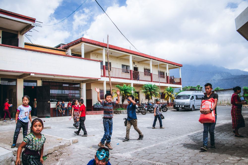 Street scene outside a red-roofed building with mountains in background.