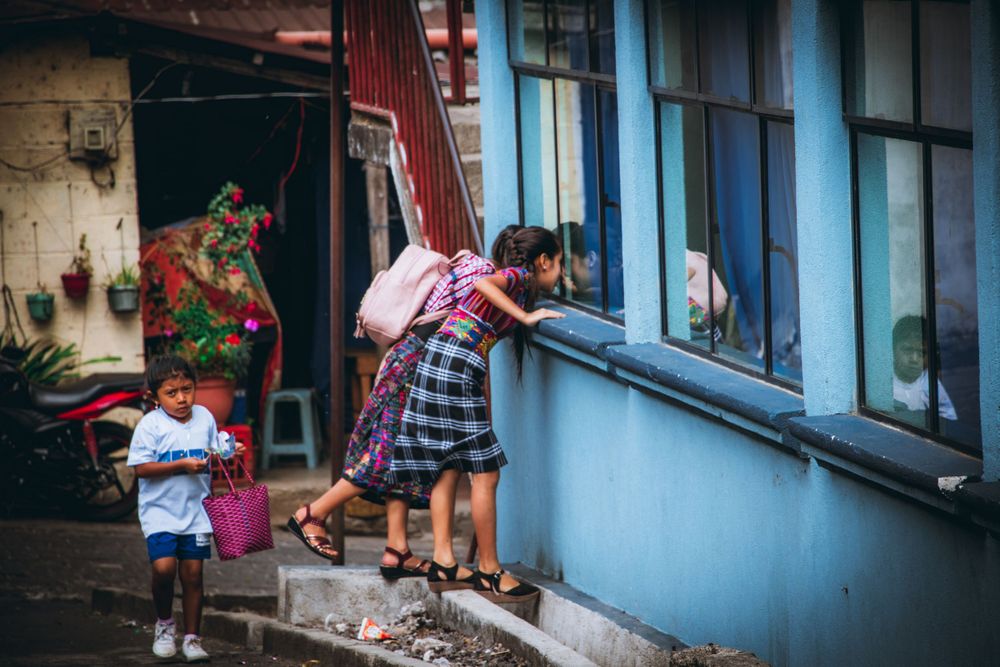 Children playing and peeking through a window of a blue building.