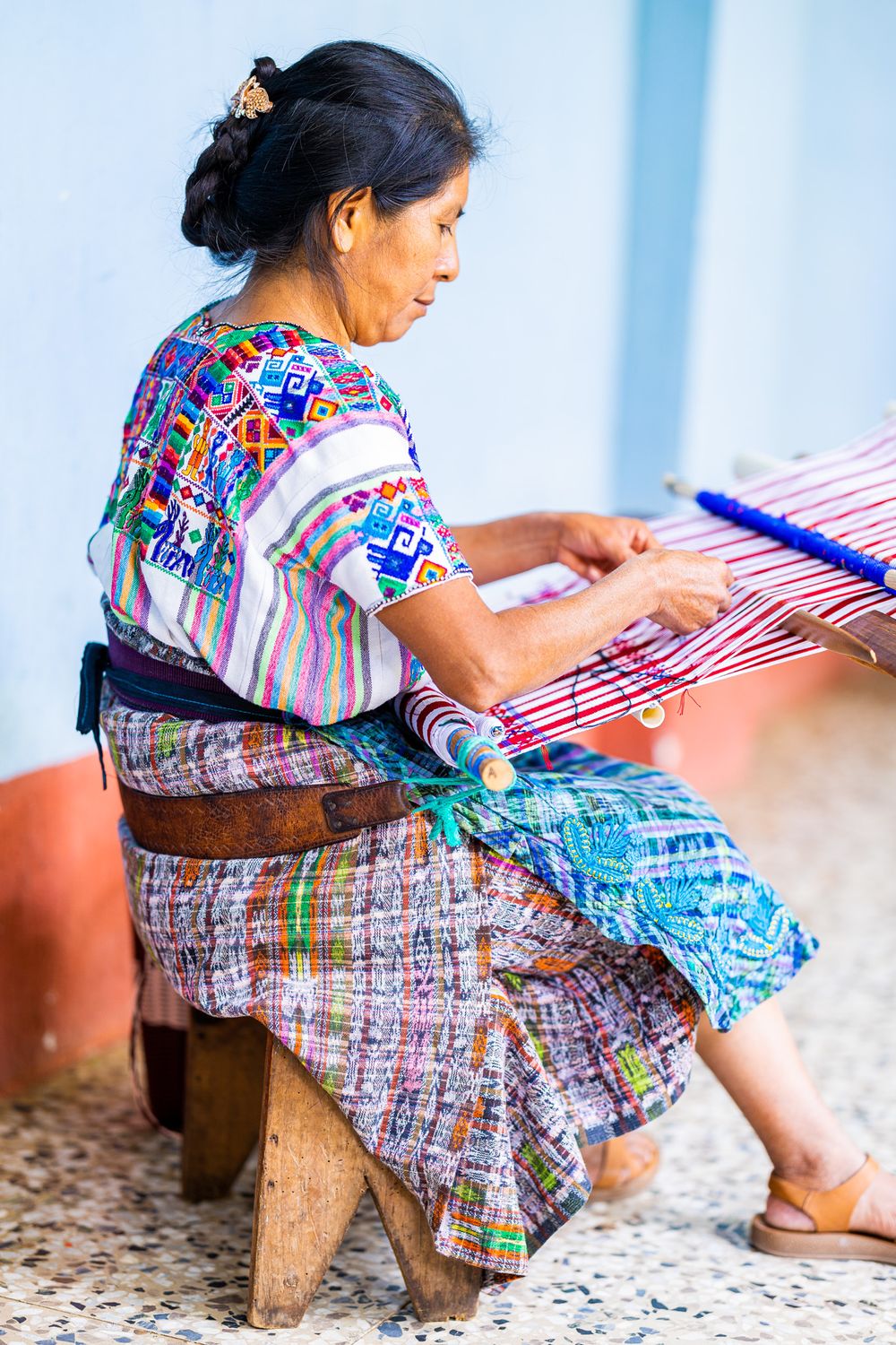 Woman in traditional Guatemalan clothing weaving on a traditional loom with colorful threads.