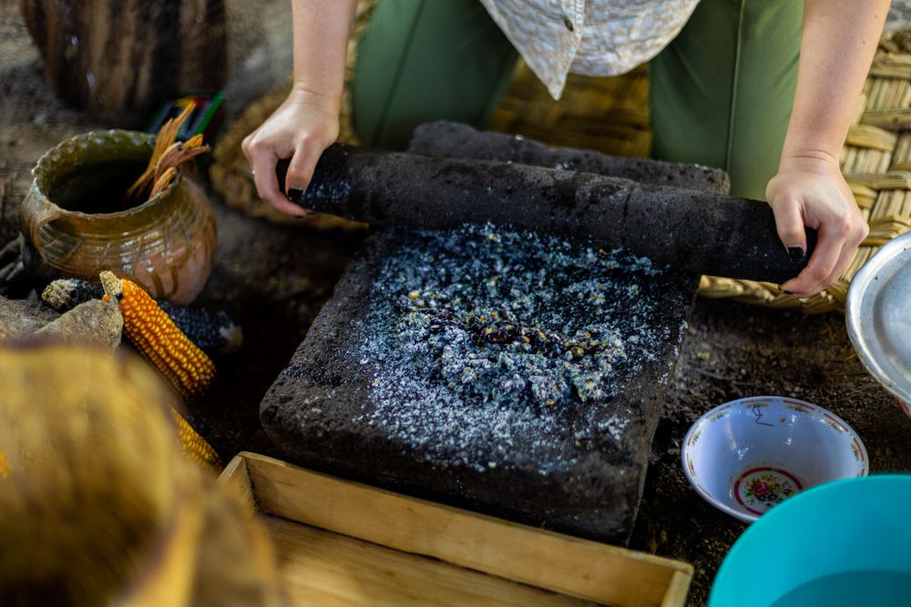 Hands preparing food on a traditional cooking surface with corn and utensils visible.