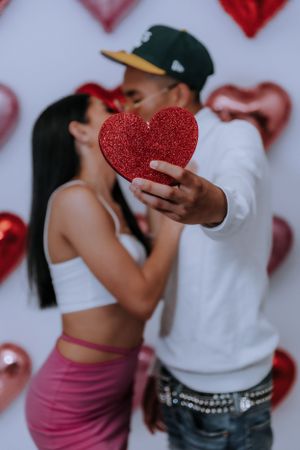 Couple poses with glittery red heart decorations against valentine backdrop.