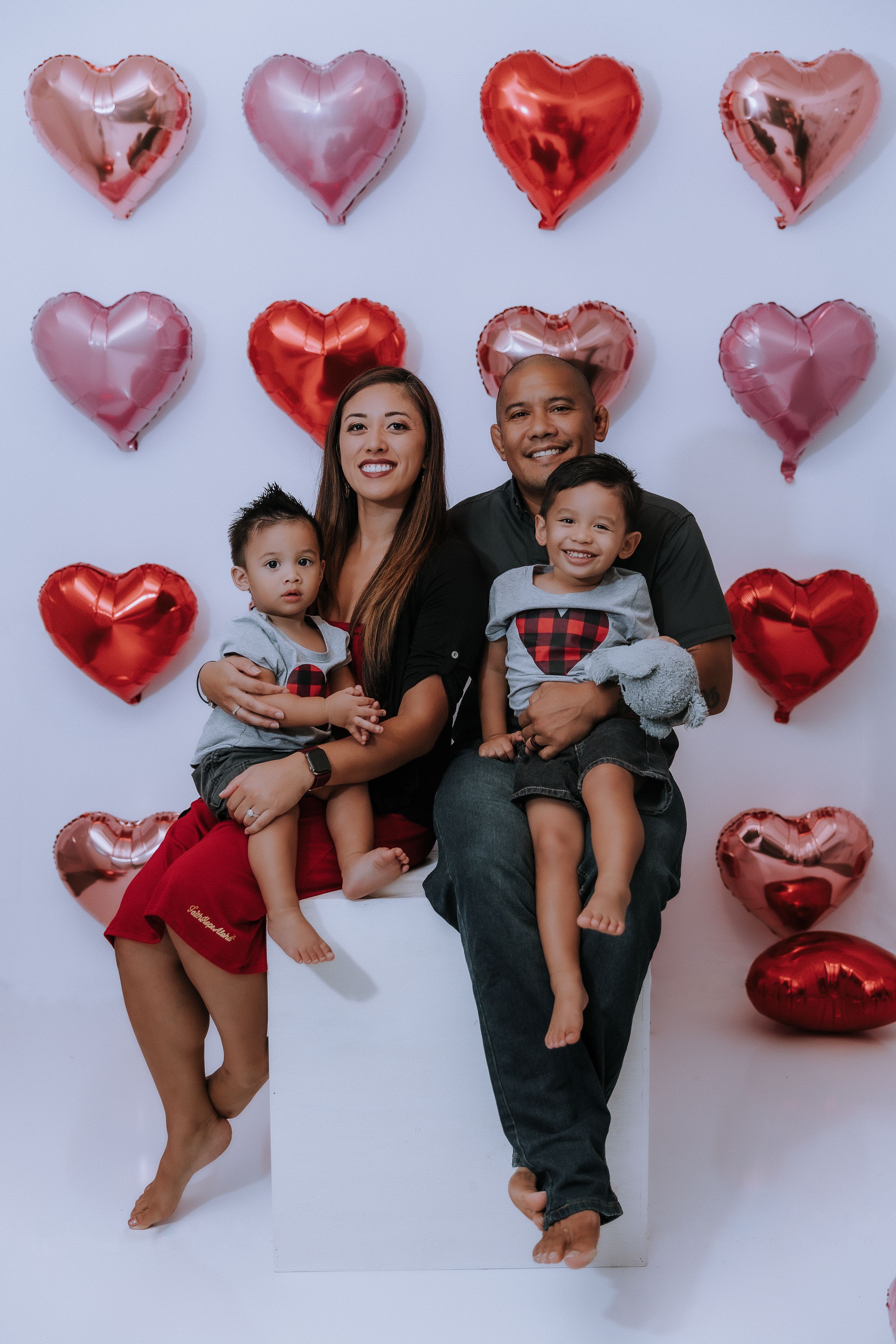 A family photo session with heart-shaped balloons featuring playful poses against a white backdrop.