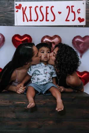 A romantic photoshoot setup with a 'Kisses 25 cents' sign and heart balloons in the background.