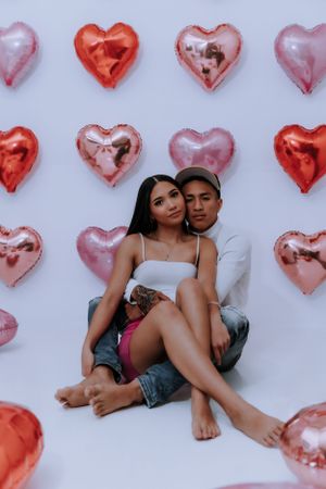 Intimate valentine photoshoot with couple against heart balloon backdrop.