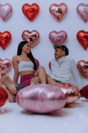 Couple relaxing on pink cushions surrounded by heart-shaped balloons.