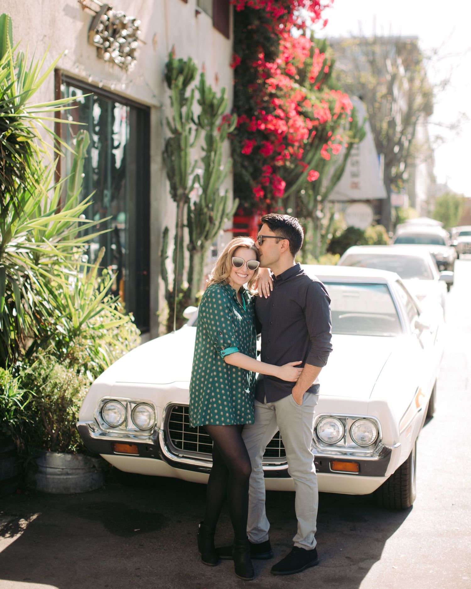 Stylish editorial couple's portrait of a man and woman posing playfully next to a classic white vintage car.