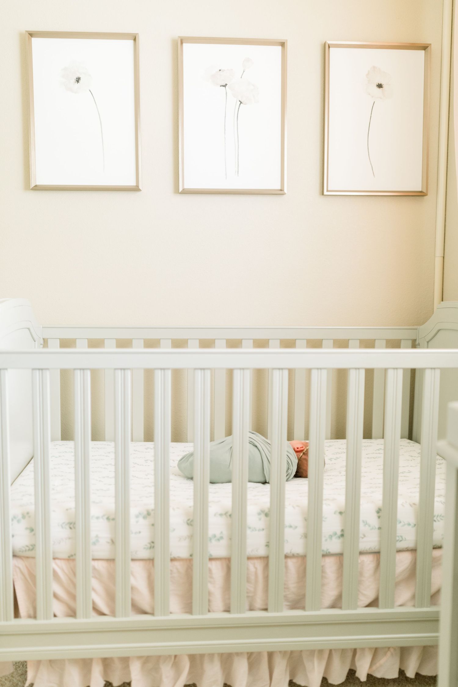 White crib with minimal floral wall art and ruffled bedskirt in peaceful nursery setting.