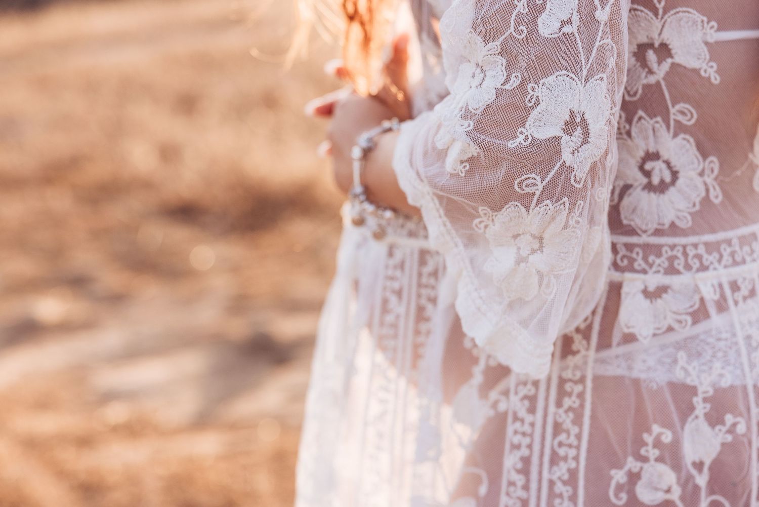 Close-up detail of delicate white lace maternity dress with floral pattern.