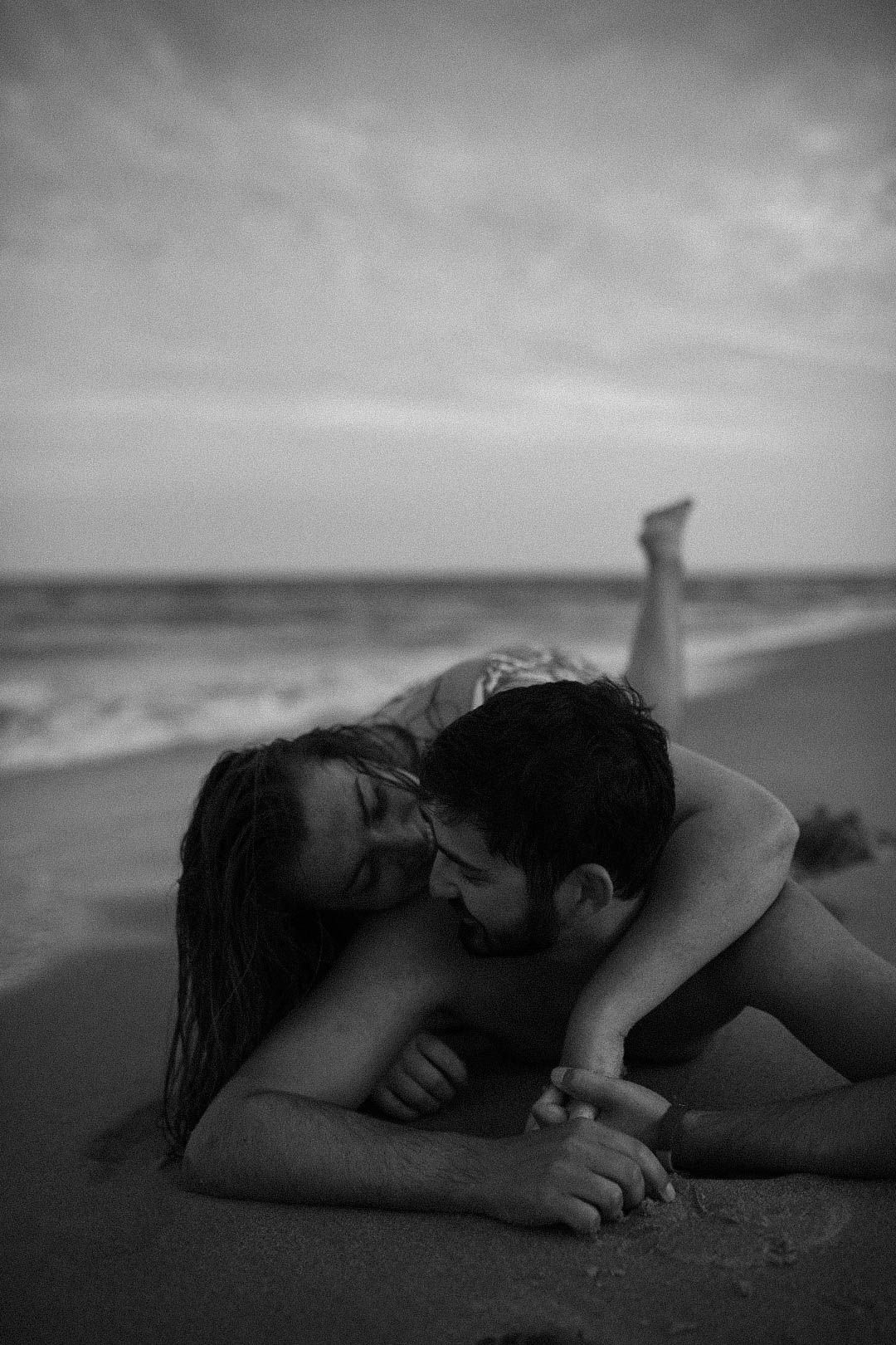 Intimate black and white photo of couple embracing on beach at sunset.