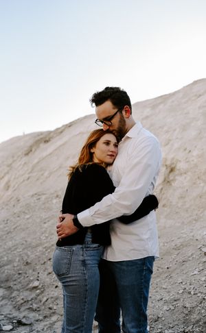 Intimate couple embracing against rocky hillside backdrop during sunset photoshoot.