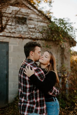 Romantic couple embracing in front of an old stone building covered in vines at sunset.