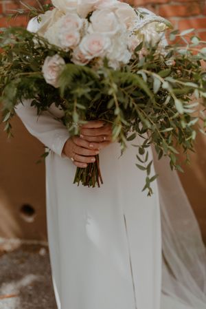 Close-up of bridal bouquet with white roses and cascading greenery against brick wall.