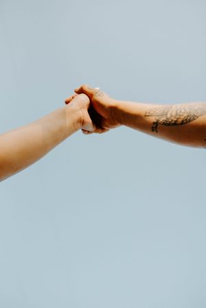 Close-up of two hands reaching and holding each other against light blue background.