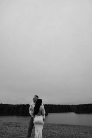 Silhouetted couple embracing by tranquil lake during overcast evening.