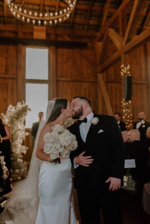 Romantic wedding ceremony in a rustic barn venue with twinkling lights and floral decorations.