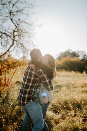Backlit couple embracing in sunny field with autumn foliage.