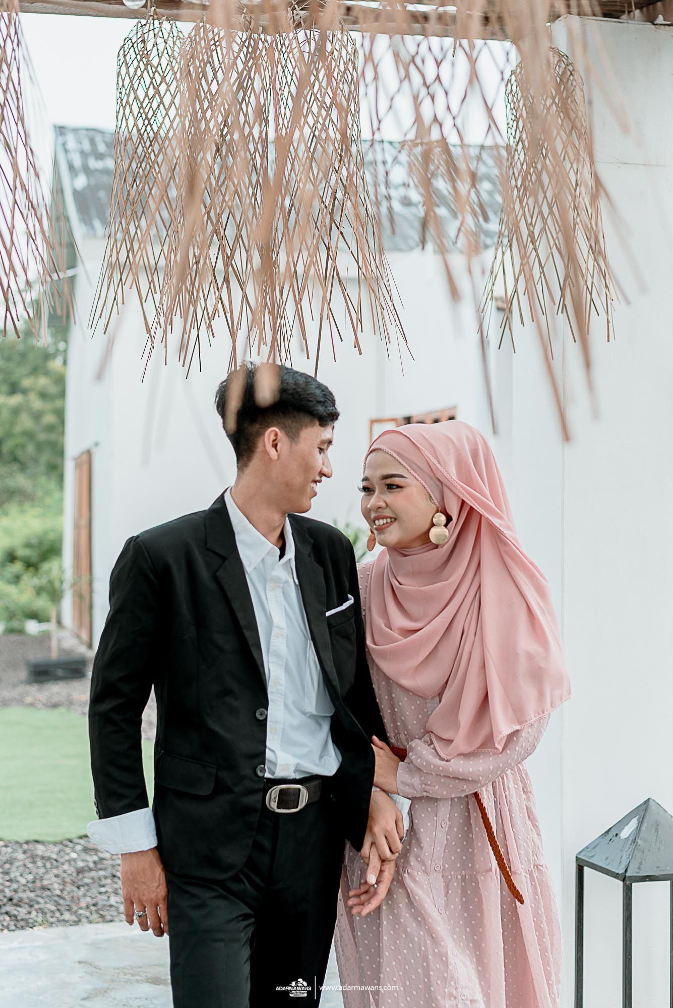 A couple in coordinated outfits shares a romantic moment under woven pendant lights.