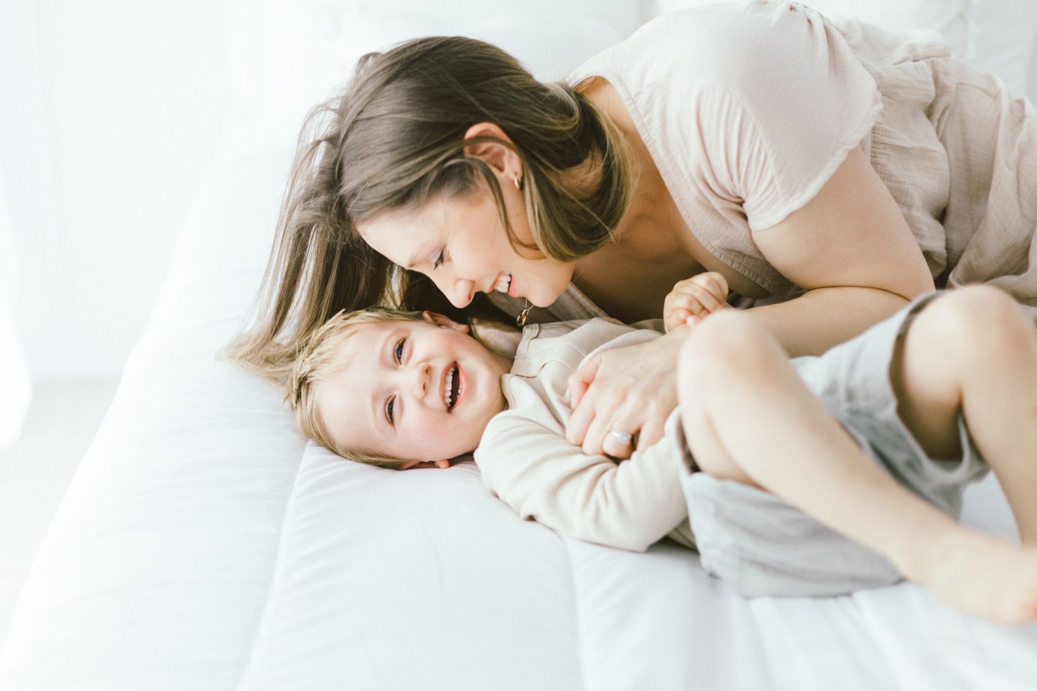 Tender moment between parent and child playing together on white sheets.